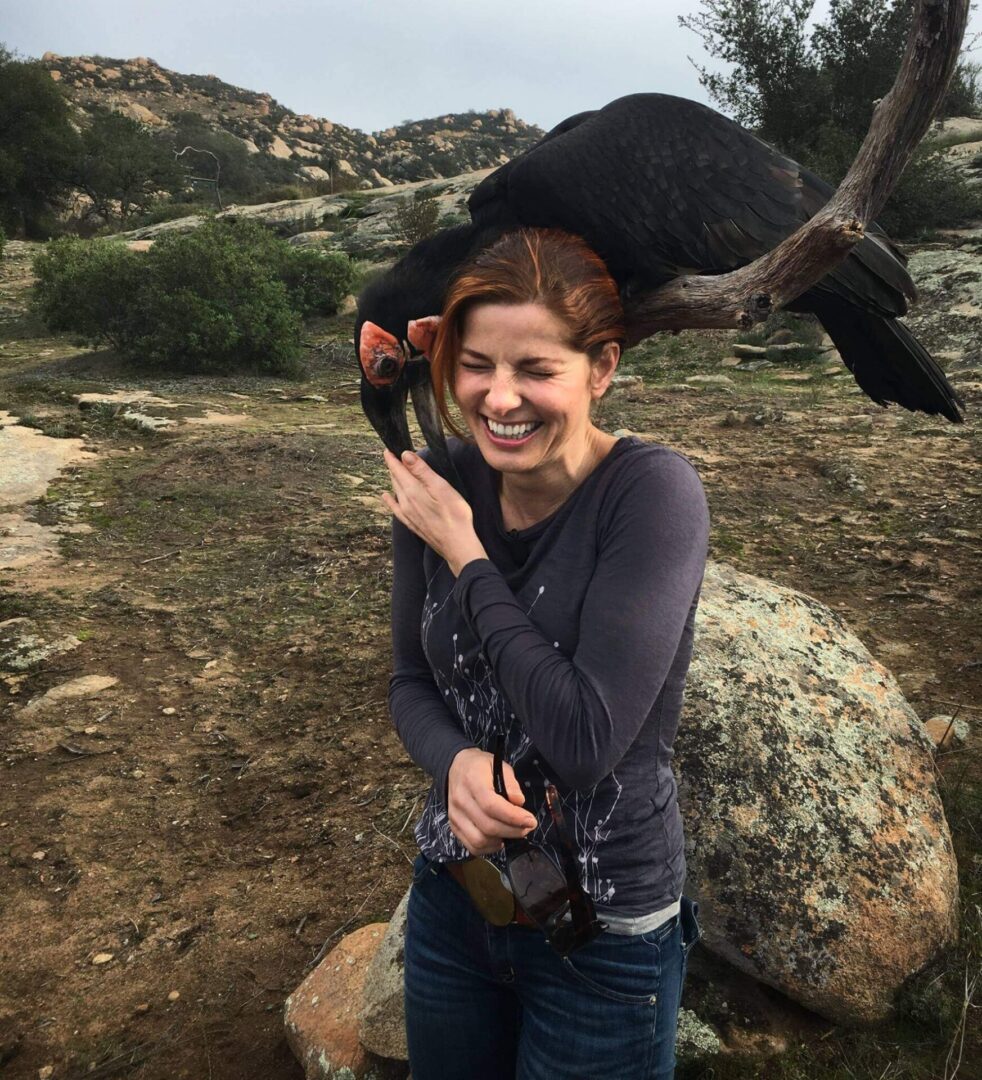 A woman holding onto a black bird on her shoulder