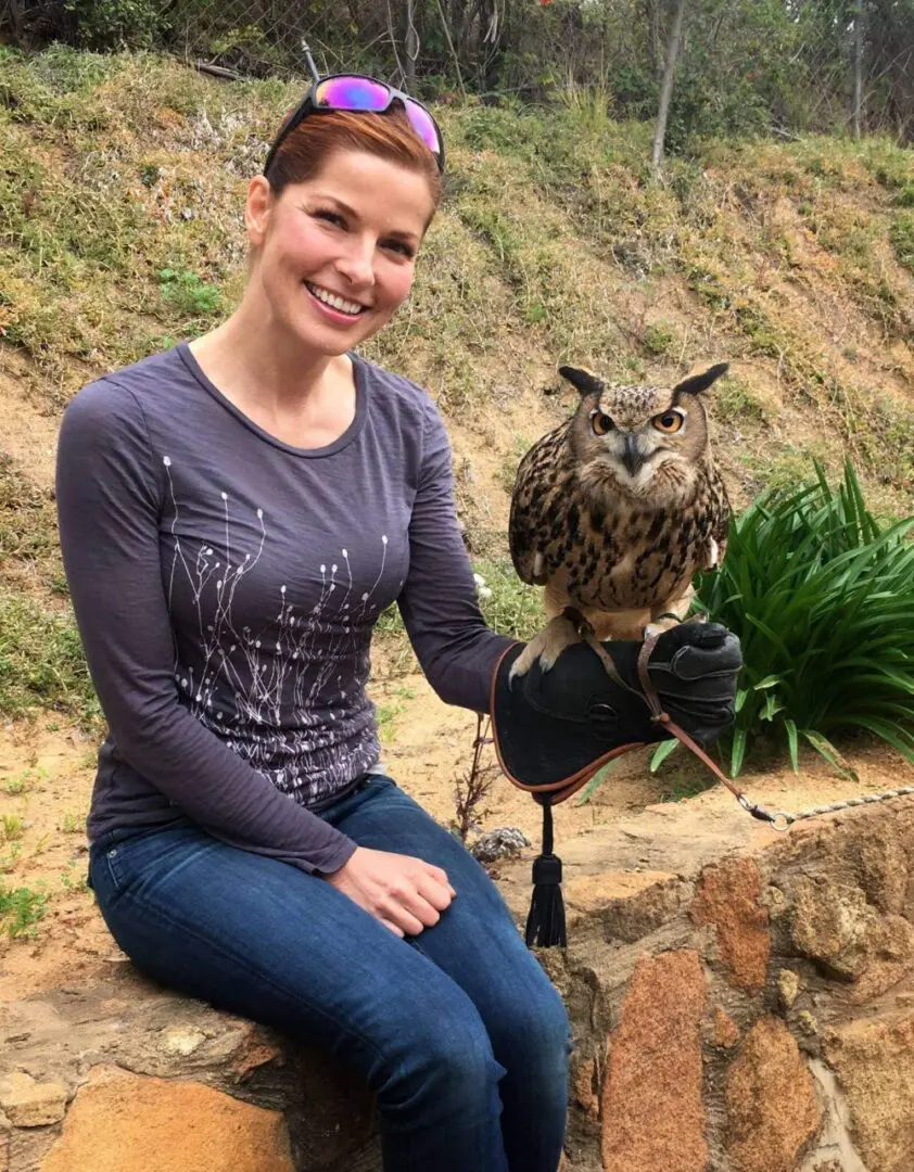 A woman sitting on the ground with an owl.