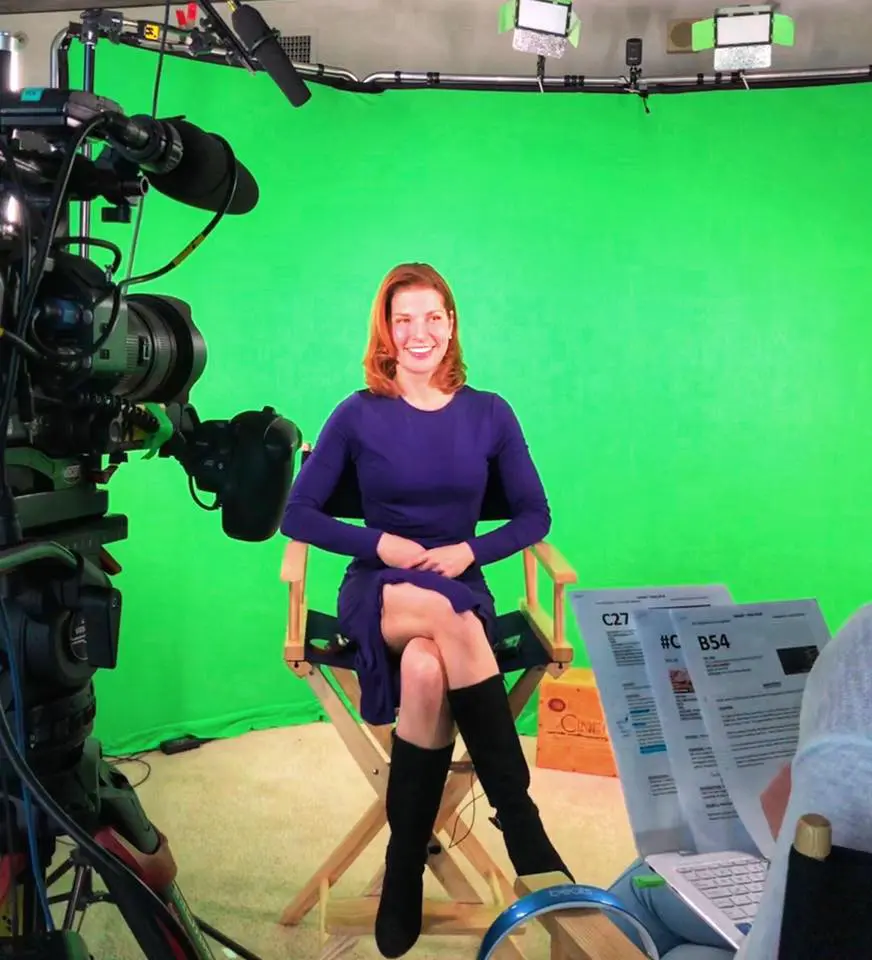 A woman sitting in front of a green screen.