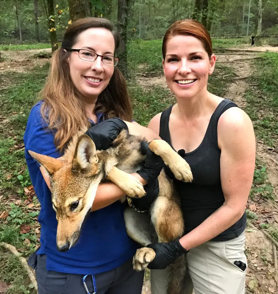 Two women holding a dog in the woods.