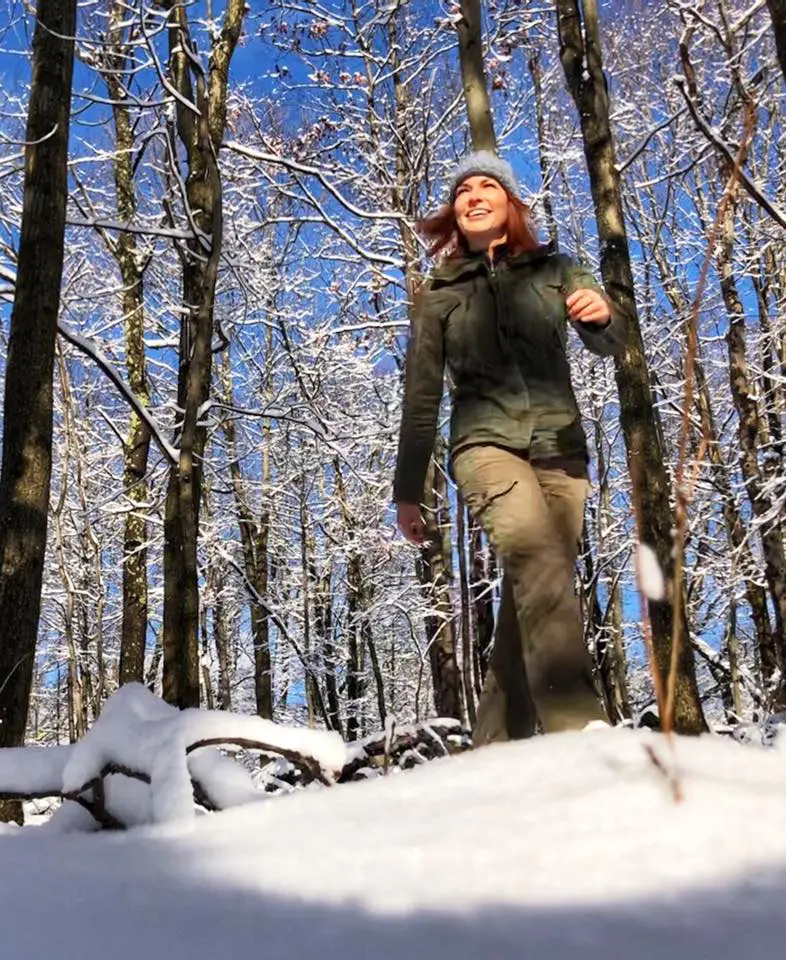 A woman is walking through the snow in her hiking gear.