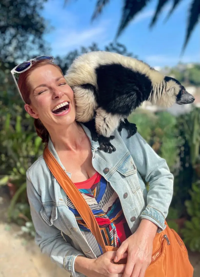 A woman holding a lemur on her shoulder.